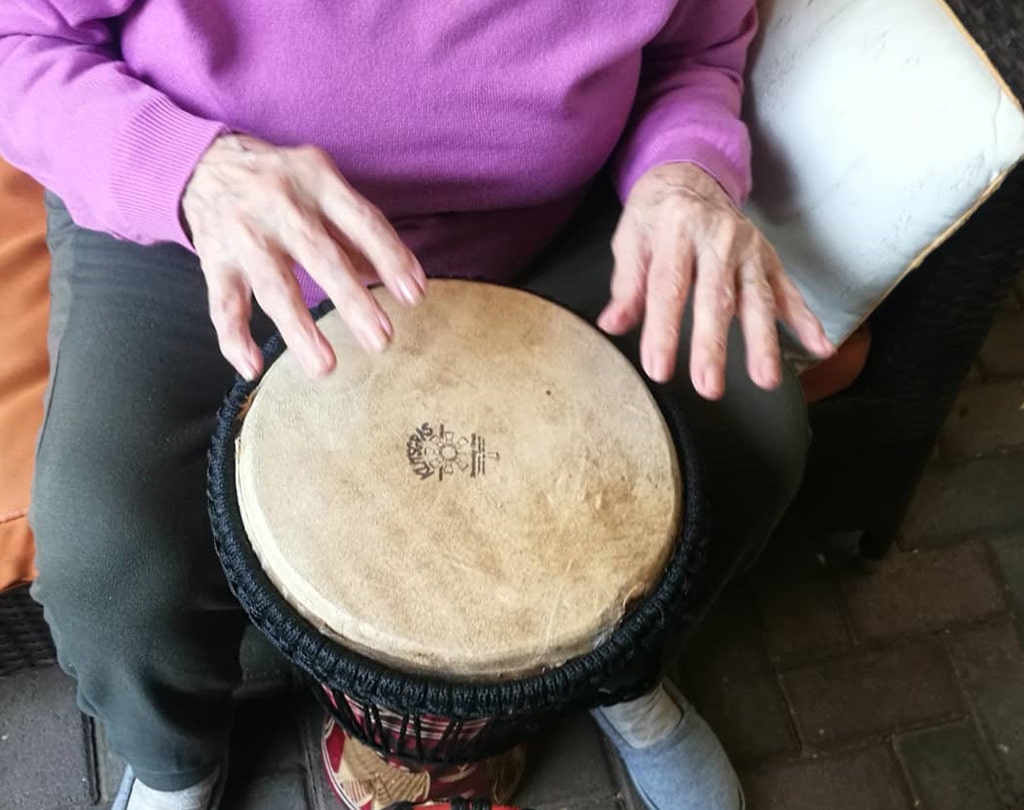 mujer mayor tocando el tambor en sesión de musicoterapia para tercera edad